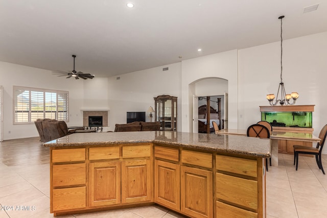 kitchen featuring light tile patterned floors, a kitchen island, decorative light fixtures, stone counters, and ceiling fan with notable chandelier