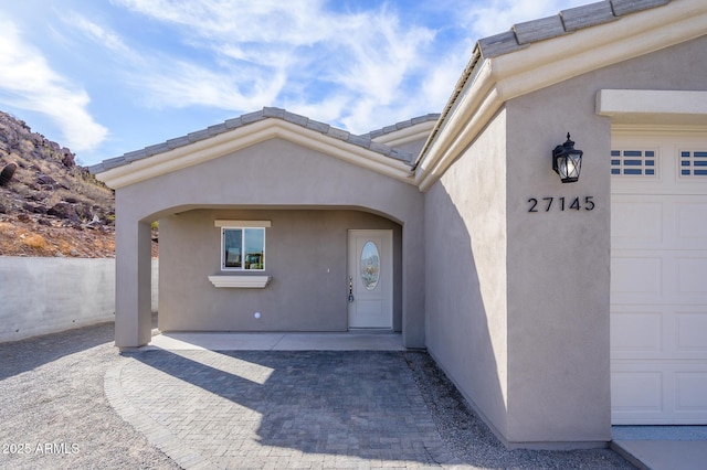 property entrance with a tiled roof, an attached garage, and stucco siding