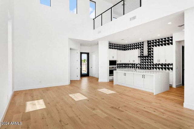 kitchen featuring white cabinetry, a high ceiling, light hardwood / wood-style flooring, oven, and a center island with sink