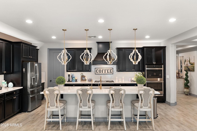 kitchen with light countertops, visible vents, appliances with stainless steel finishes, premium range hood, and a kitchen breakfast bar