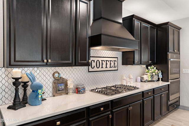 kitchen featuring stainless steel appliances, light countertops, backsplash, custom exhaust hood, and light wood finished floors