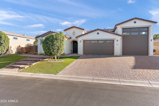 mediterranean / spanish home with a garage, decorative driveway, a front yard, and stucco siding