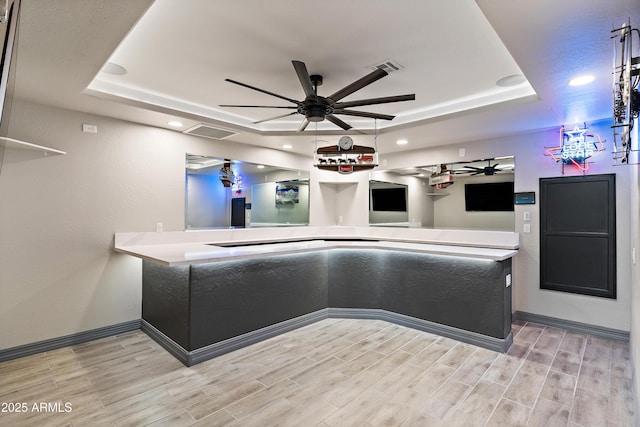 kitchen featuring baseboards, a raised ceiling, ceiling fan, light countertops, and wood finish floors