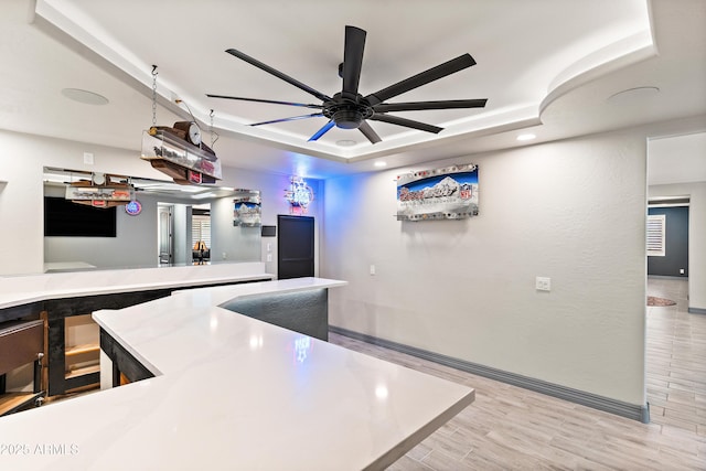 kitchen with baseboards, a raised ceiling, a ceiling fan, light countertops, and light wood-style floors