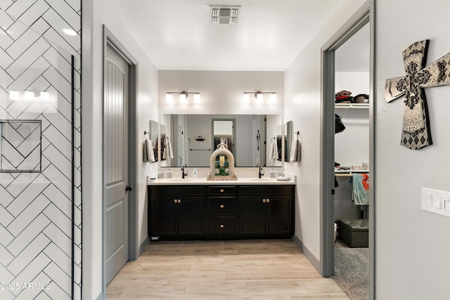 full bath featuring a walk in closet, double vanity, visible vents, a sink, and wood finished floors