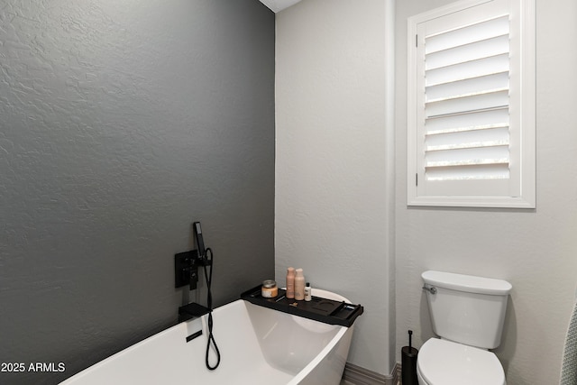 bathroom with a textured wall, a freestanding tub, and toilet