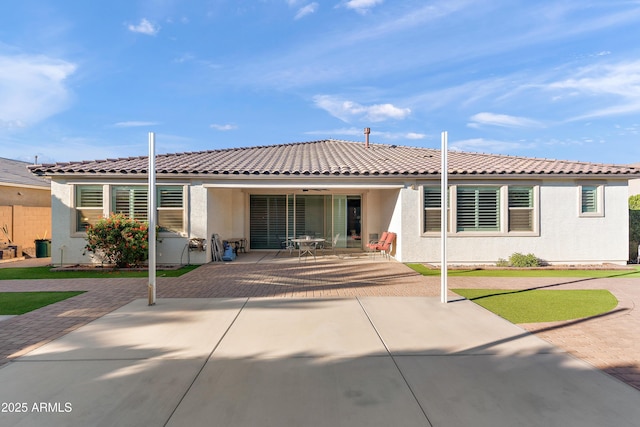 rear view of property with a patio, a tile roof, and stucco siding