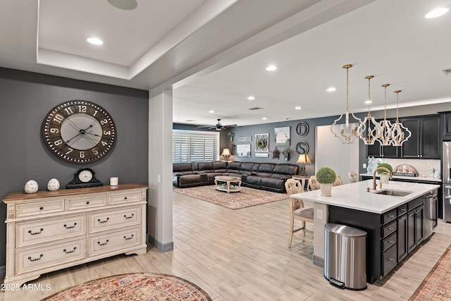 kitchen with a breakfast bar area, dark cabinets, a sink, light countertops, and light wood-type flooring