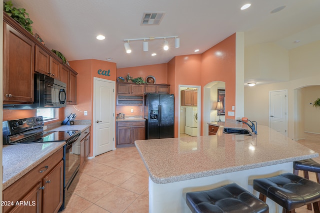 kitchen with light stone countertops, sink, black appliances, washer / clothes dryer, and a breakfast bar area