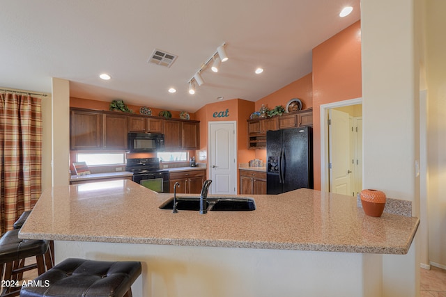 kitchen with kitchen peninsula, vaulted ceiling, sink, black appliances, and a breakfast bar area