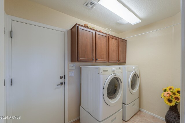 laundry room featuring washer and dryer, light tile patterned floors, a textured ceiling, and cabinets