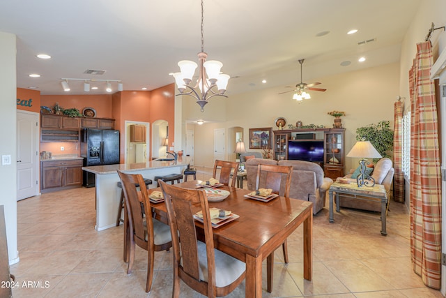 dining space featuring ceiling fan with notable chandelier, light tile patterned floors, sink, and a high ceiling