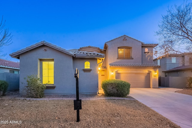 mediterranean / spanish-style house featuring an attached garage, fence, a tile roof, concrete driveway, and stucco siding