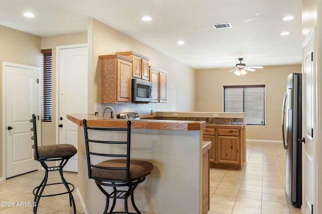 kitchen featuring ceiling fan, light tile patterned floors, appliances with stainless steel finishes, a kitchen bar, and kitchen peninsula