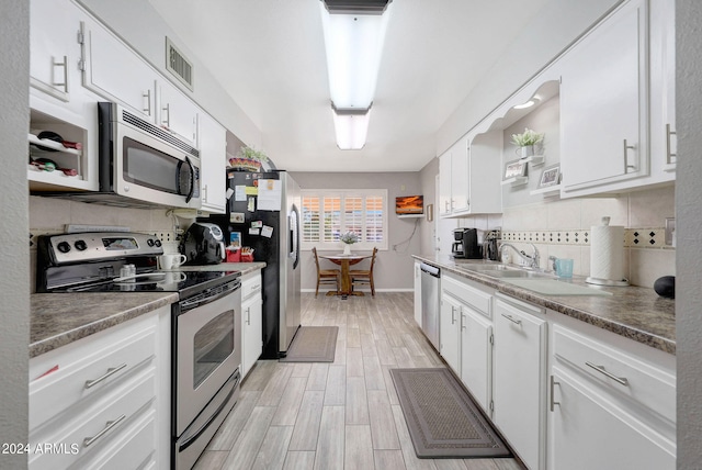 kitchen featuring sink, light wood-type flooring, white cabinetry, appliances with stainless steel finishes, and tasteful backsplash