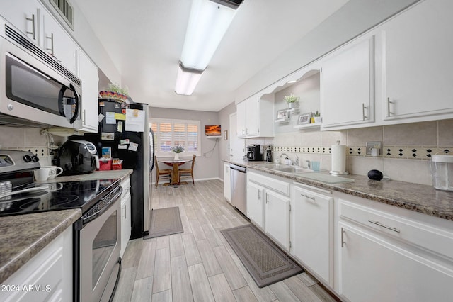 kitchen featuring appliances with stainless steel finishes, sink, backsplash, white cabinets, and light hardwood / wood-style flooring