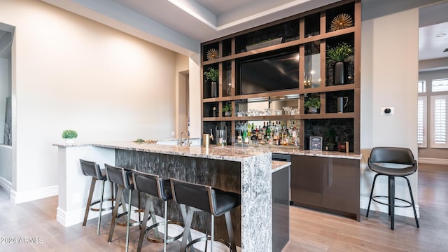 bar with indoor wet bar, a sink, baseboards, and light wood-type flooring