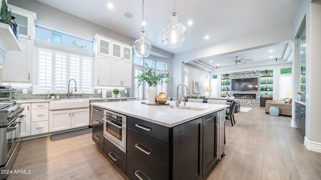 kitchen with ceiling fan, a warm lit fireplace, white cabinetry, a sink, and stainless steel appliances