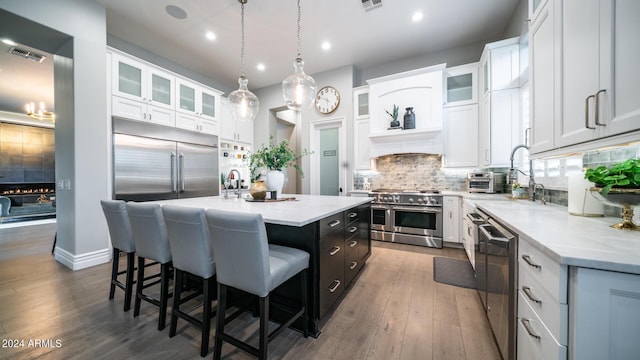 kitchen with white cabinets, a breakfast bar, high end appliances, a kitchen island, and visible vents