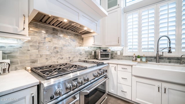 kitchen featuring a sink, white cabinetry, premium range hood, and double oven range
