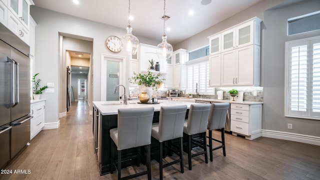 kitchen featuring light countertops, a kitchen breakfast bar, a kitchen island with sink, stainless steel built in fridge, and tasteful backsplash