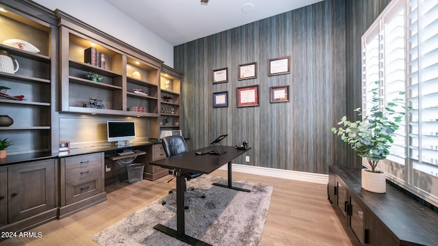 office featuring baseboards, built in desk, wallpapered walls, and light wood-style flooring