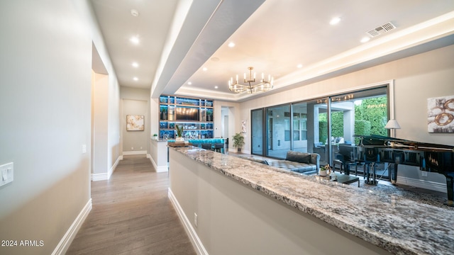 hallway with a notable chandelier, a raised ceiling, recessed lighting, wood finished floors, and visible vents