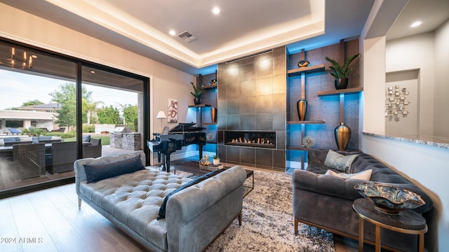 living area featuring visible vents, wood finished floors, recessed lighting, a raised ceiling, and a tiled fireplace