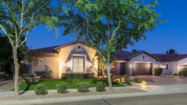 view of front of property featuring a tile roof, a garage, stucco siding, concrete driveway, and a yard