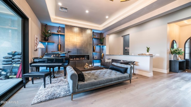 sitting room with visible vents, a tiled fireplace, wood finished floors, baseboards, and a tray ceiling