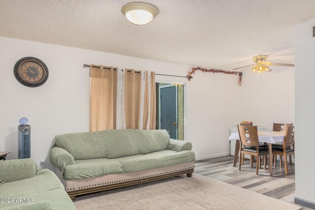 living room with light wood-type flooring, ceiling fan, and a textured ceiling