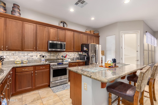 kitchen with backsplash, a kitchen island, a breakfast bar, light stone countertops, and stainless steel appliances