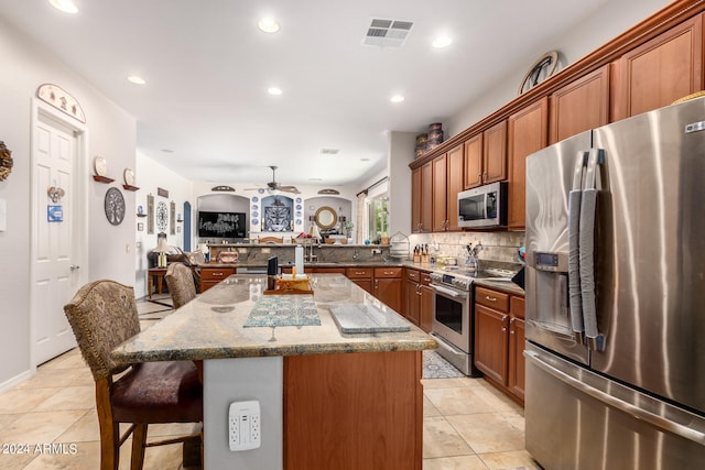 kitchen featuring a kitchen island, a breakfast bar area, kitchen peninsula, appliances with stainless steel finishes, and light stone counters