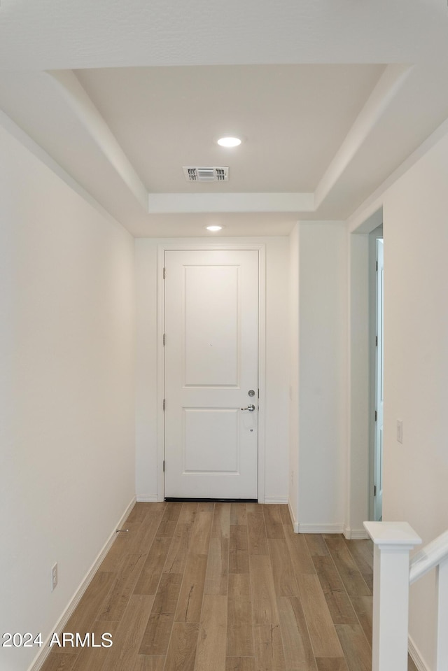 corridor featuring light wood-type flooring and a raised ceiling