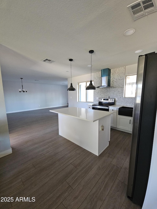 kitchen featuring white cabinets, a center island, wall chimney range hood, stainless steel appliances, and hanging light fixtures