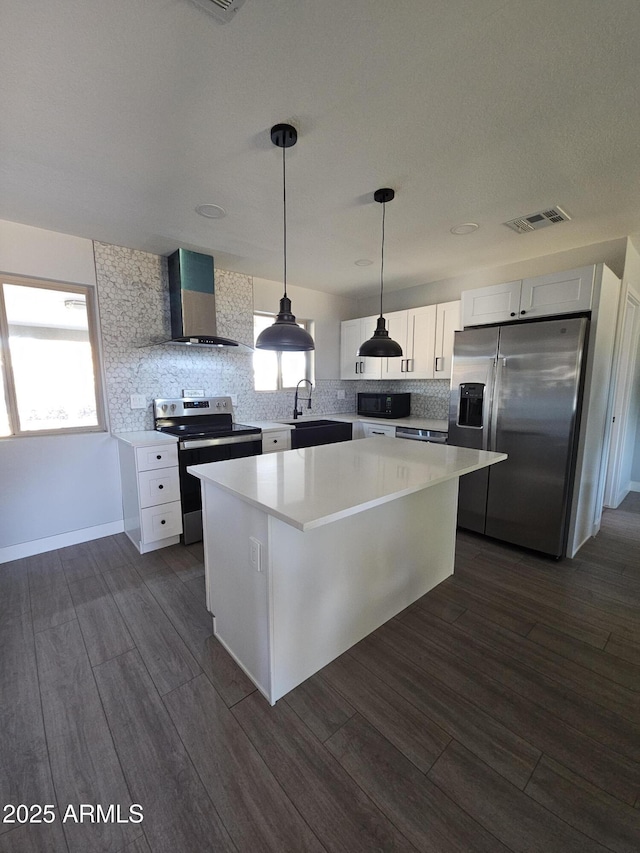 kitchen with stainless steel appliances, wall chimney exhaust hood, white cabinetry, and a center island