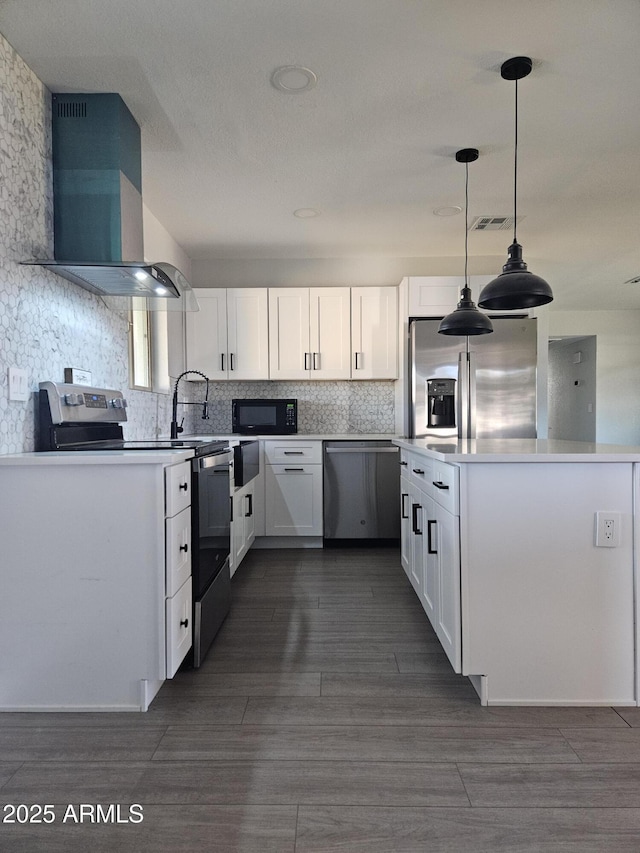 kitchen with decorative light fixtures, appliances with stainless steel finishes, wall chimney range hood, and white cabinetry