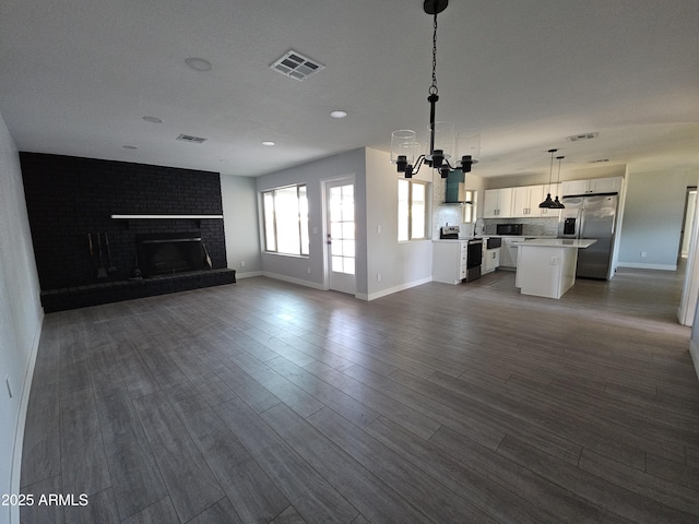 unfurnished living room with a brick fireplace, dark hardwood / wood-style floors, and a notable chandelier