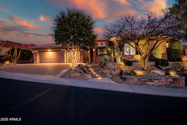 view of front of home with decorative driveway, stone siding, an attached garage, and stucco siding