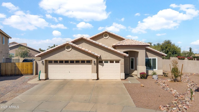 mediterranean / spanish home featuring fence, a tiled roof, concrete driveway, stucco siding, and an attached garage