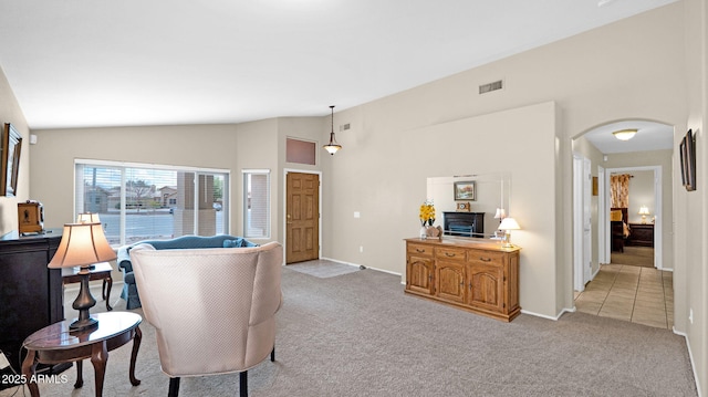 living area with lofted ceiling, arched walkways, visible vents, and light carpet