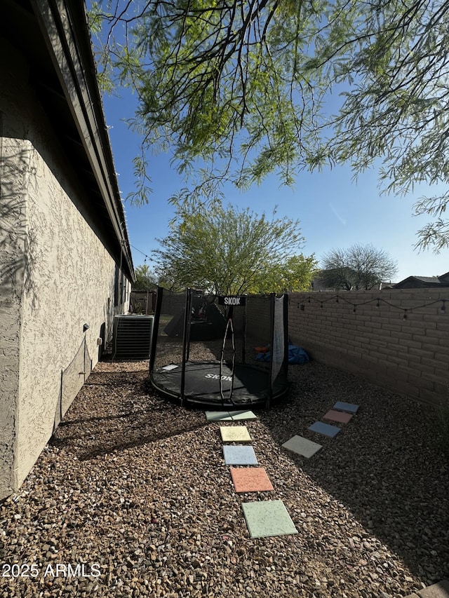 view of yard featuring a fenced backyard, a trampoline, and central AC unit