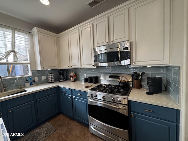 kitchen with a sink, stainless steel appliances, visible vents, decorative backsplash, and blue cabinets