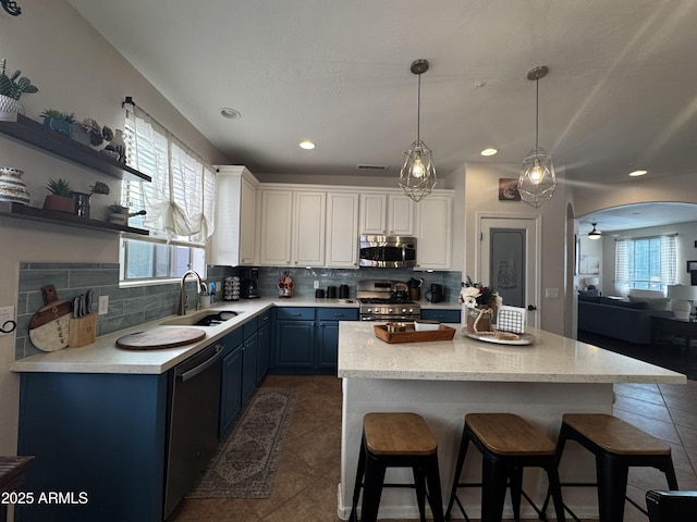 kitchen featuring blue cabinets, a sink, decorative backsplash, arched walkways, and stainless steel appliances