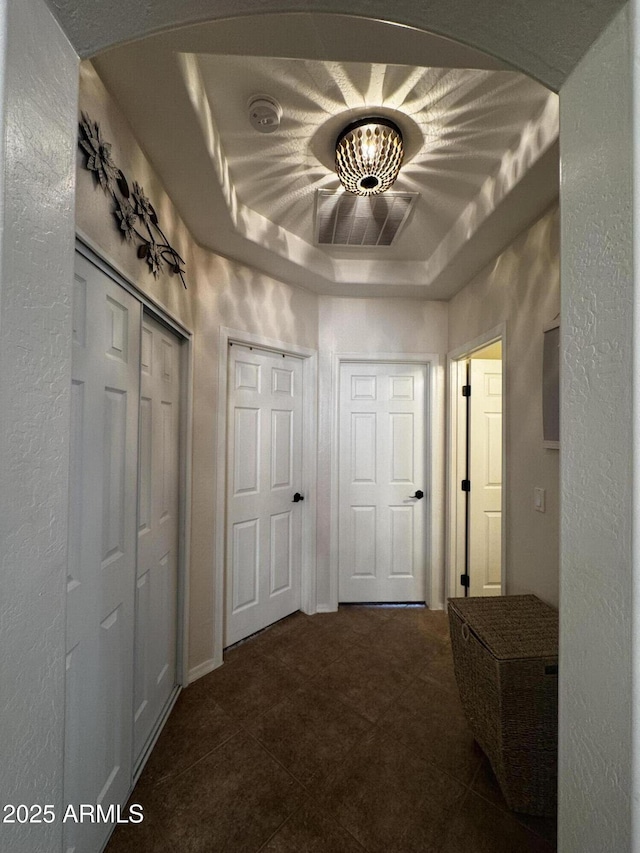 hall featuring a raised ceiling, dark tile patterned floors, arched walkways, and a textured wall