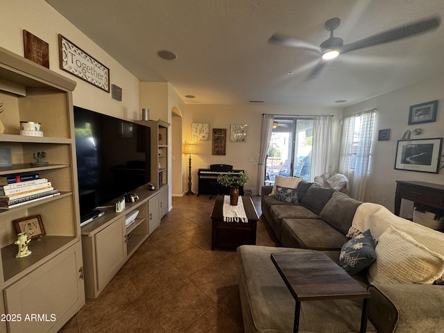 living area featuring dark tile patterned flooring, a ceiling fan, and arched walkways