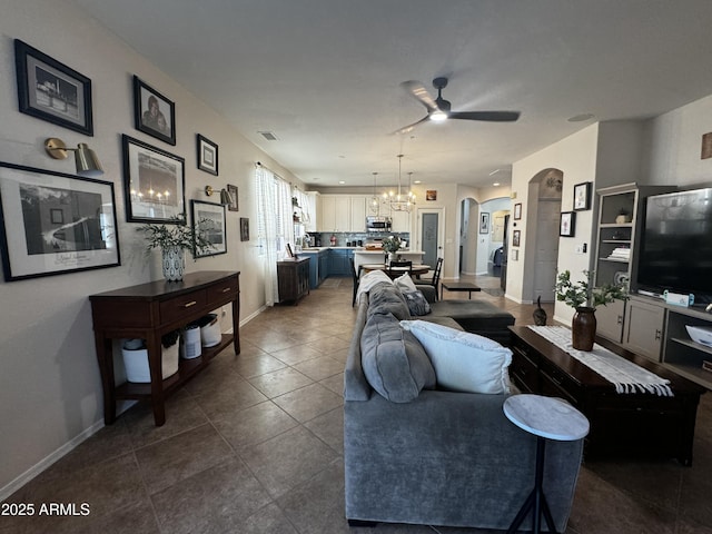living room with baseboards, visible vents, ceiling fan with notable chandelier, dark tile patterned flooring, and arched walkways