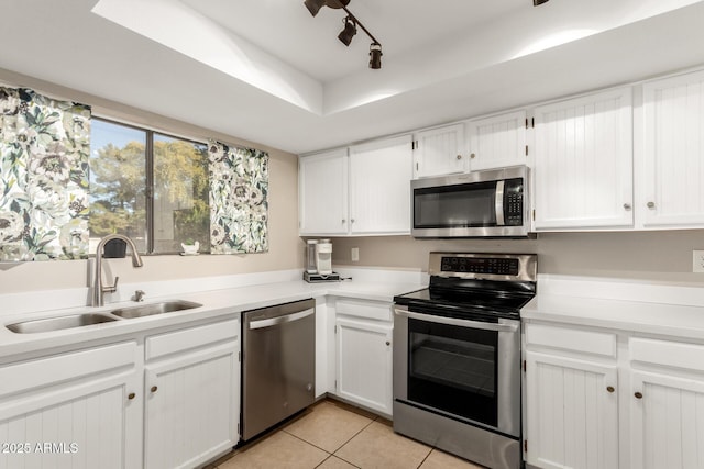 kitchen featuring sink, white cabinets, light tile patterned floors, track lighting, and appliances with stainless steel finishes