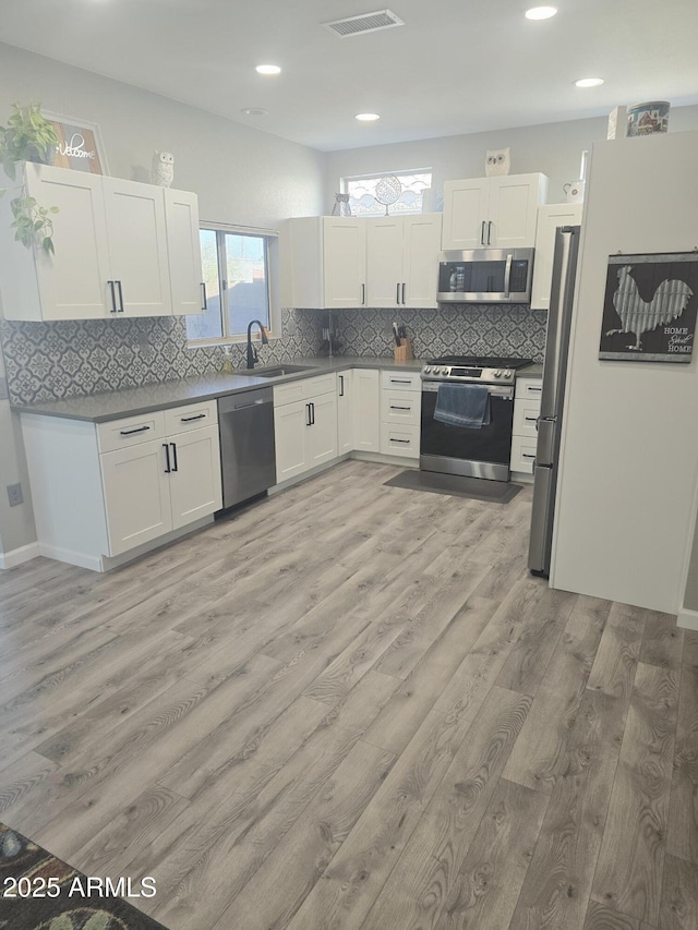 kitchen featuring appliances with stainless steel finishes, light wood-type flooring, a sink, and white cabinetry