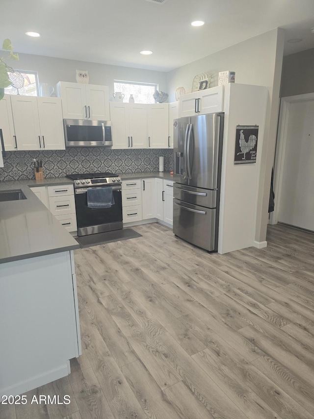 kitchen featuring light wood finished floors, stainless steel appliances, a wealth of natural light, tasteful backsplash, and white cabinetry